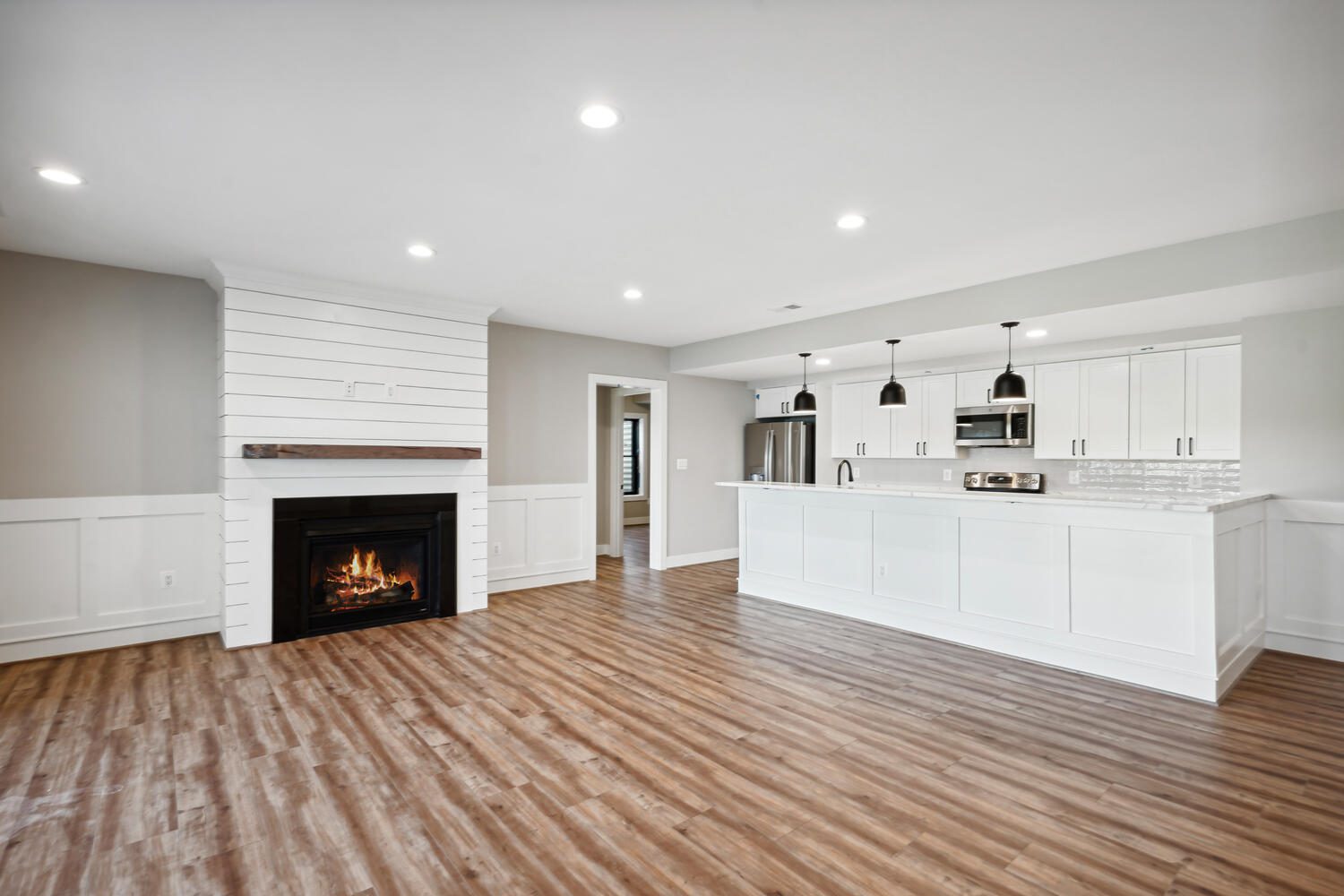 Spacious open-concept living area with wood floors, a fireplace, recessed lighting, and a modern kitchen featuring white cabinets and pendant lights.
