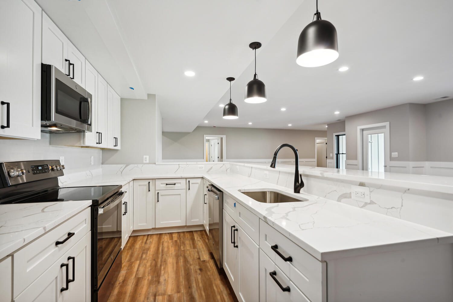 Modern kitchen with white cabinetry, marble countertops, stainless steel appliances, black fixtures, pendant lighting, and wood flooring.