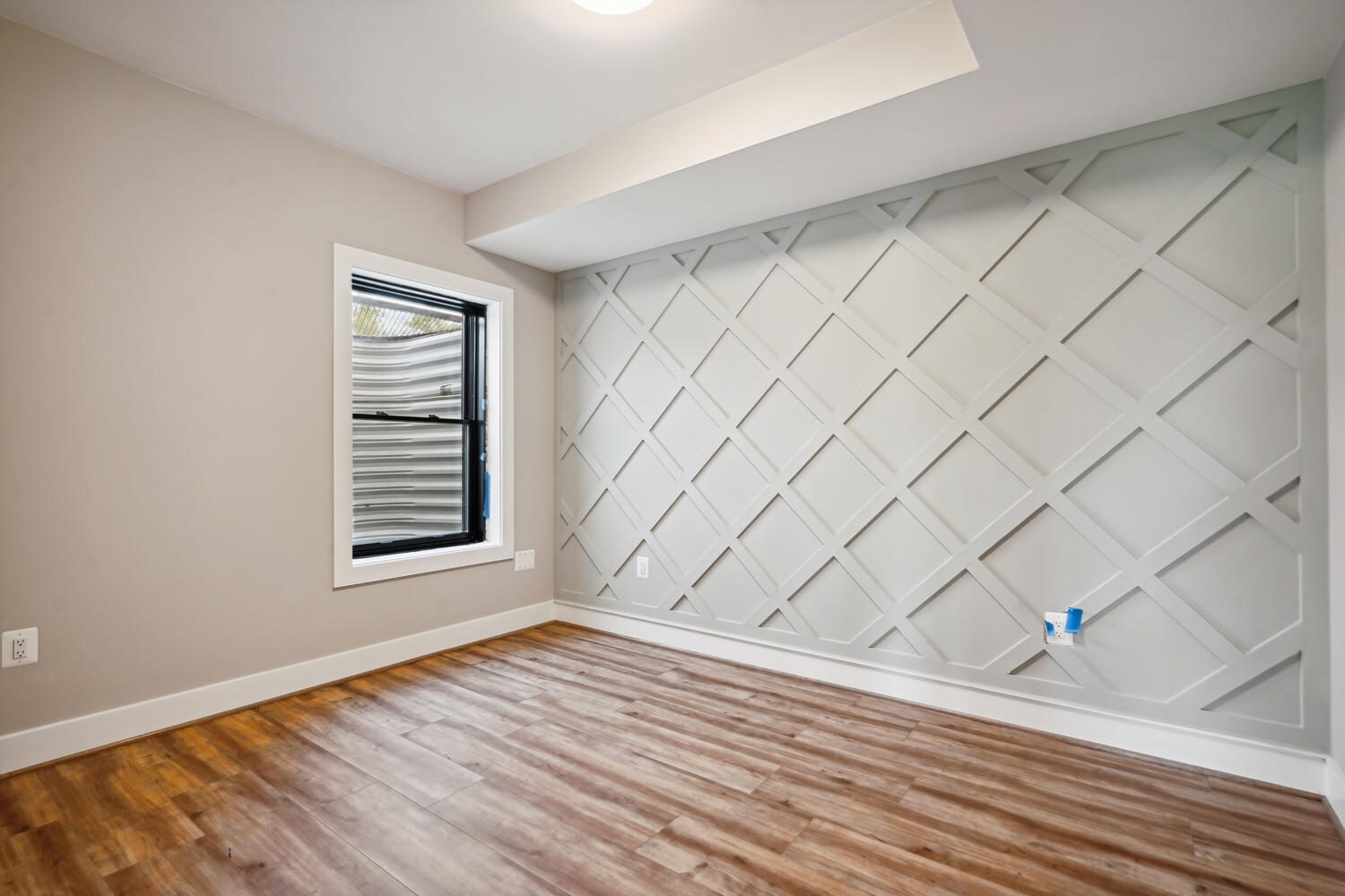 Empty room with wooden floor and a window. The back wall features a geometric lattice design in a light color.