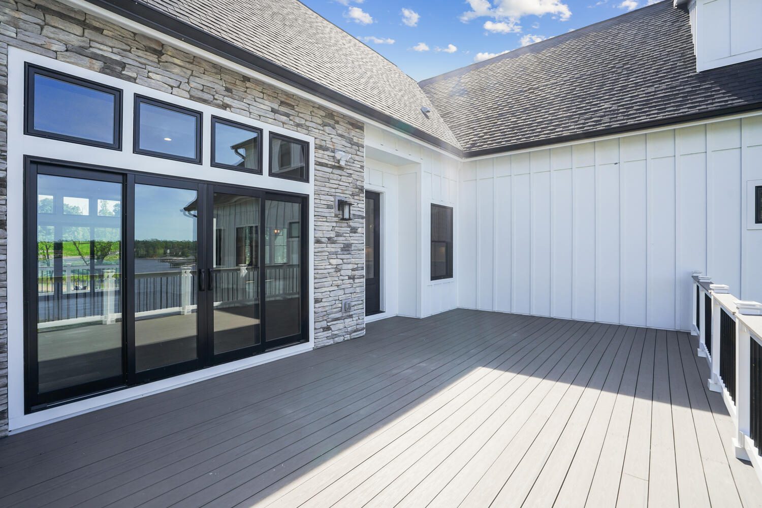 Spacious rooftop deck with wood flooring, modern glass doors, and a mix of stone and white walls, overlooking a scenic view.