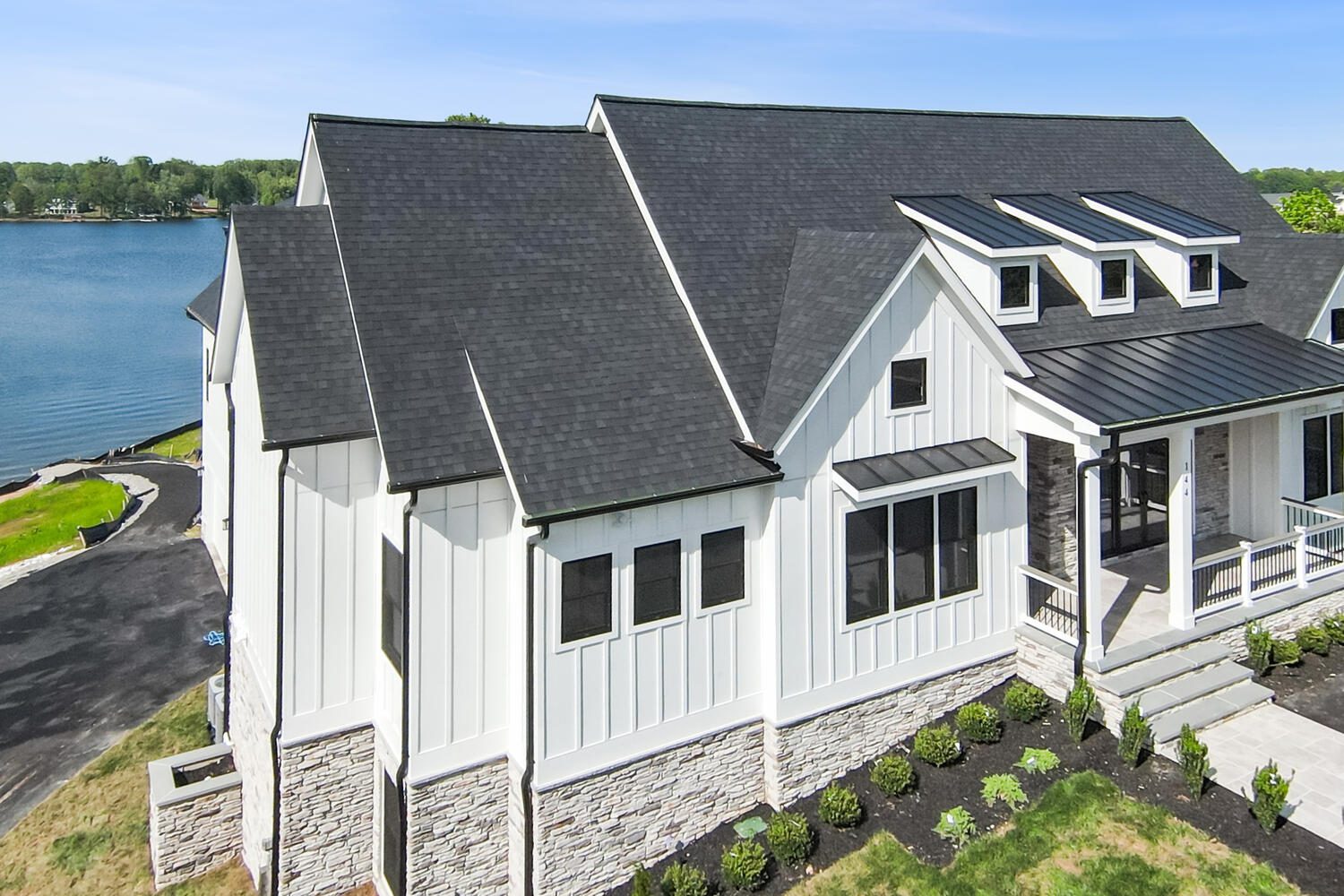 Modern white house with dark roof near a lake, featuring multiple gables, large windows, and a landscaped yard.