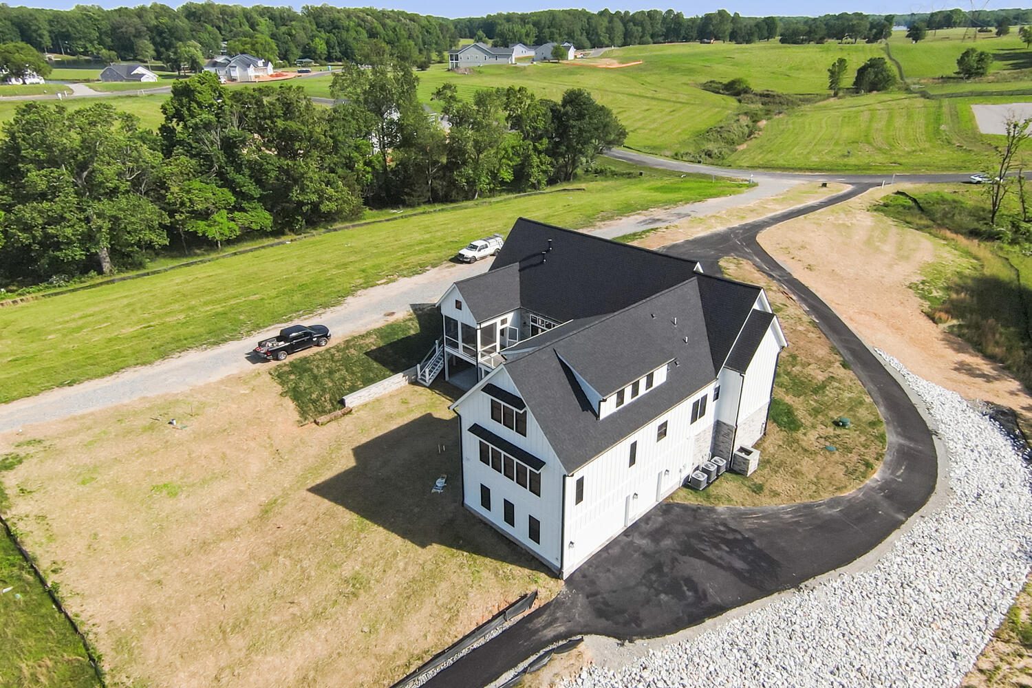 Aerial view of a large white house with a dark roof, surrounded by grassy land and trees, with a driveway leading to the house.