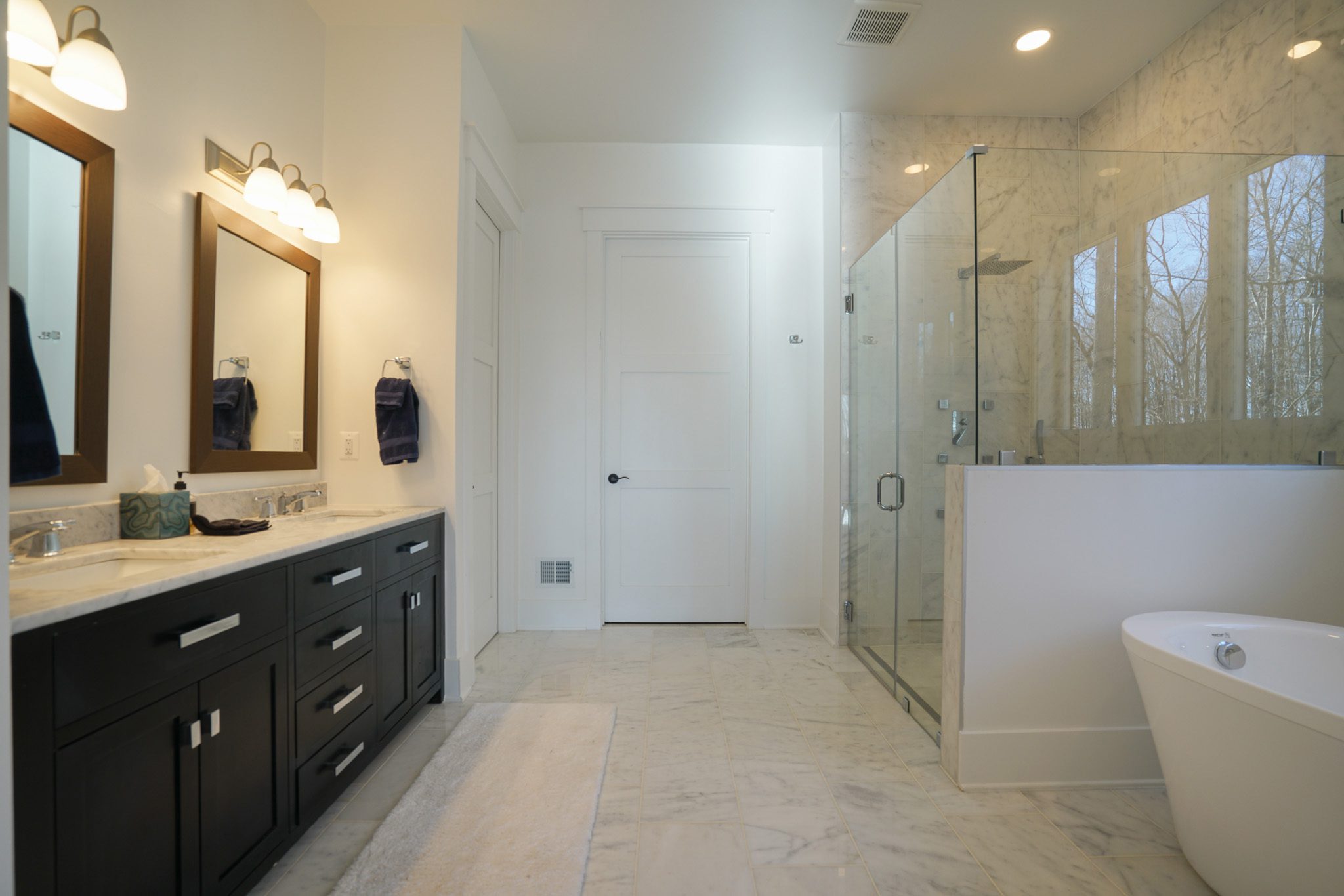 A modern bathroom with double sinks, a large mirror, a glass-enclosed shower, and a freestanding bathtub on a marble floor.