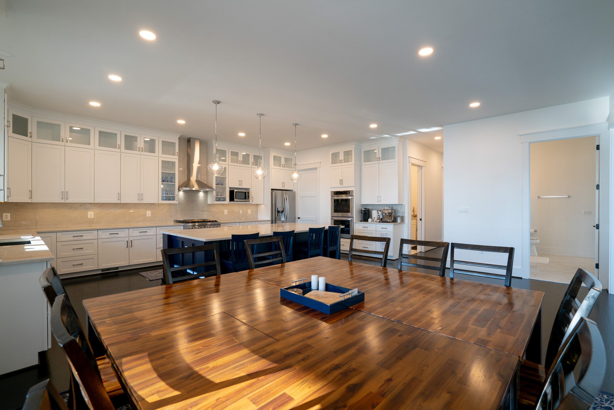 Spacious modern kitchen and dining area with a wooden table, black chairs, white cabinetry, stainless steel appliances, and recessed lighting.