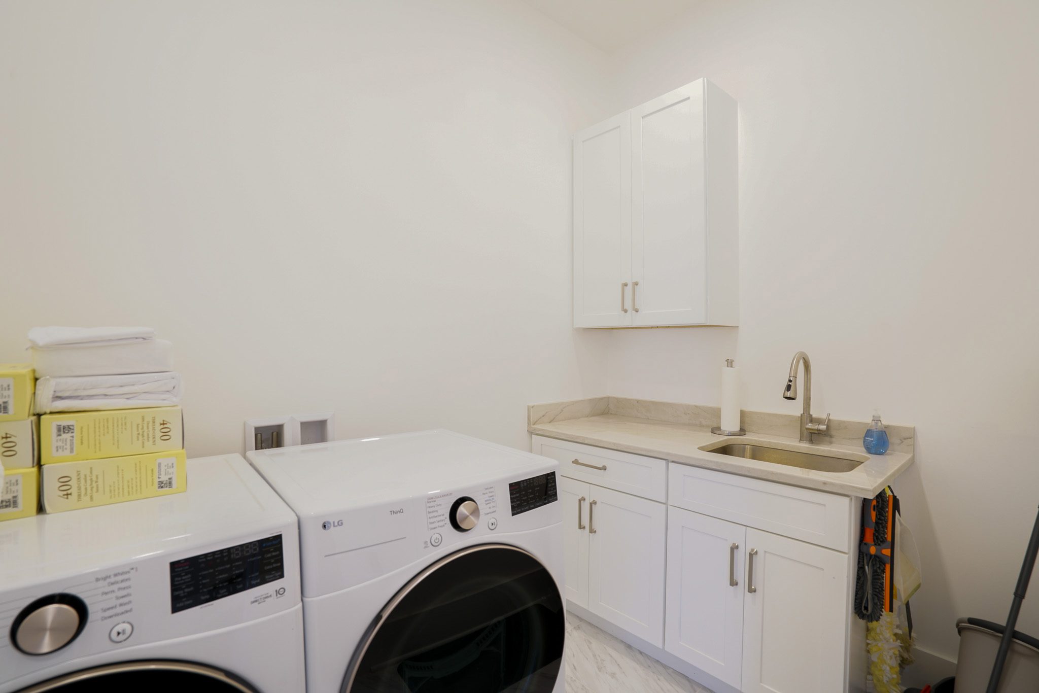 Laundry room with a front-loading washer and dryer, countertop with a sink, stacked towels, and cleaning supplies.