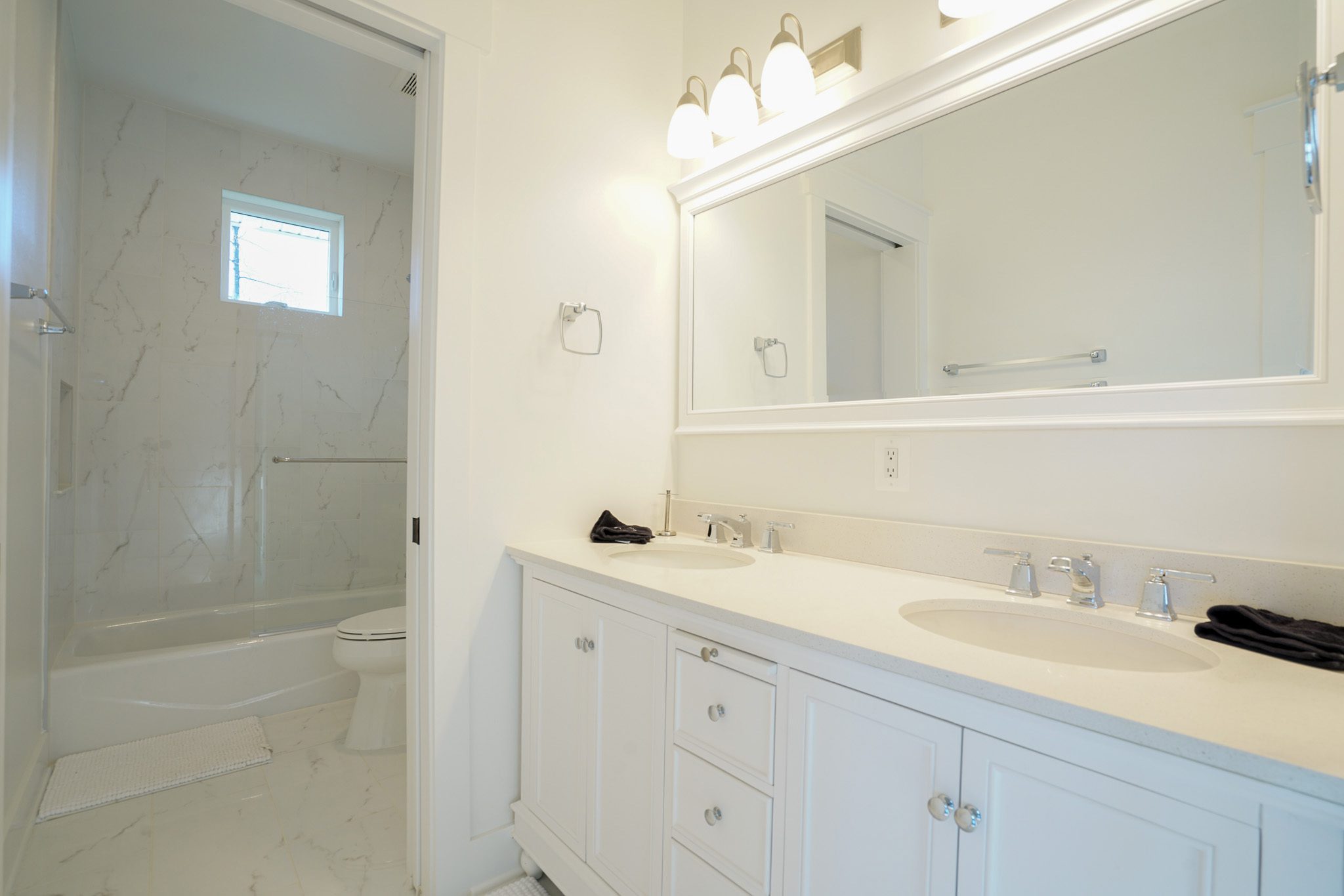 Bathroom with a white double-sink vanity, large mirror, and a bathtub with a shower. Light fixtures are above the mirror, and there's a window in the shower area.