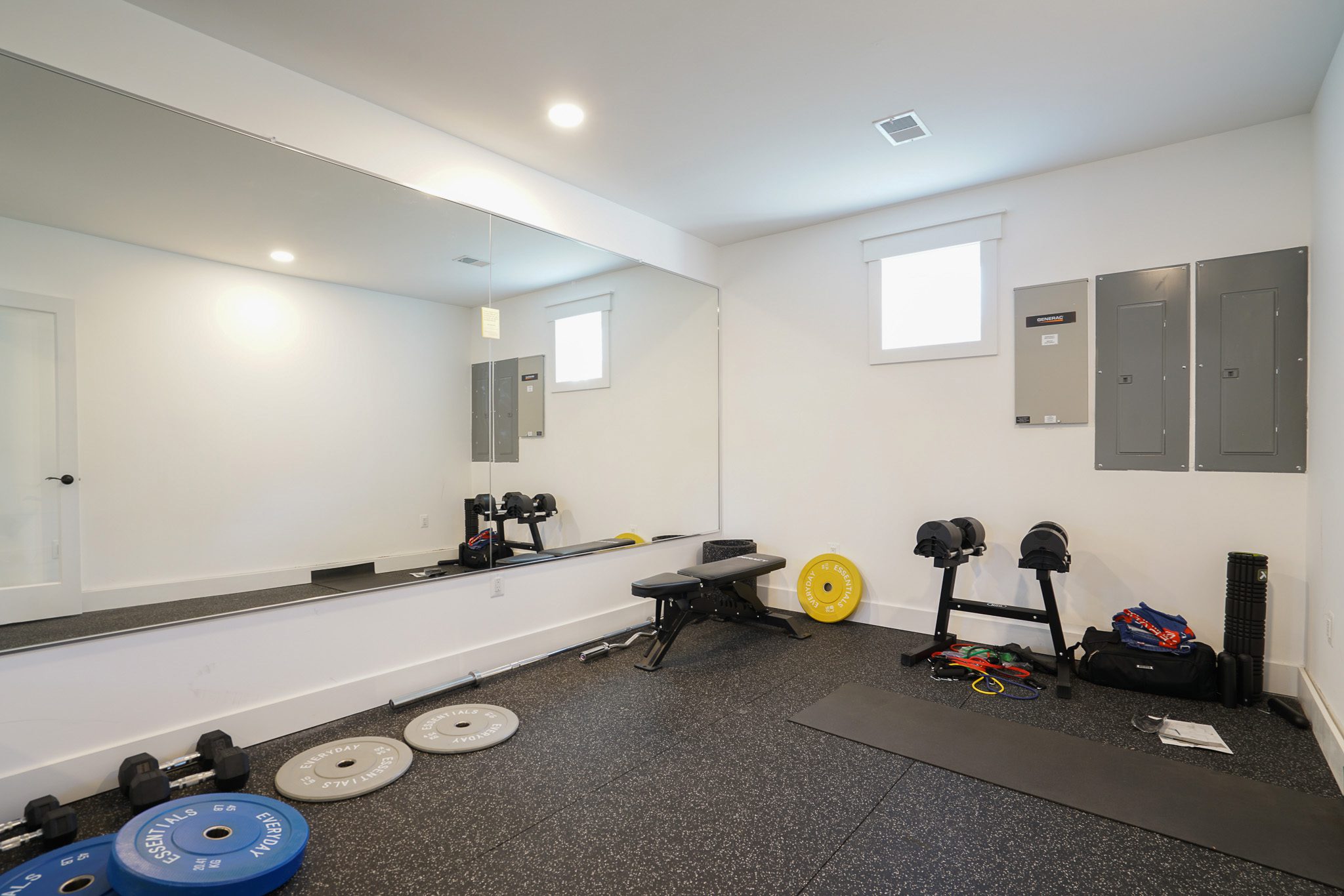 Home gym with weights, bench, exercise equipment on rubber flooring, and a large mirror on the wall.
