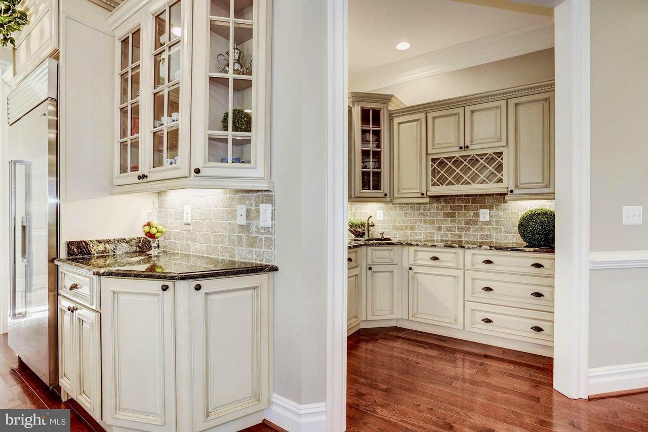 Modern kitchen with white cabinetry, granite countertops, tile backsplash, and wood flooring. Upper cabinets have glass doors, and a built-in wine rack is visible.