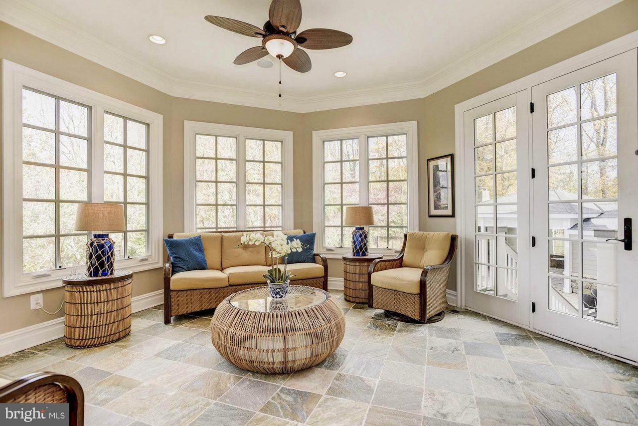 Bright sunroom with large windows, tile floor, ceiling fan, and patio doors. Furnished with wicker chairs, a sofa, round coffee table, and lamps. Neutral color scheme.