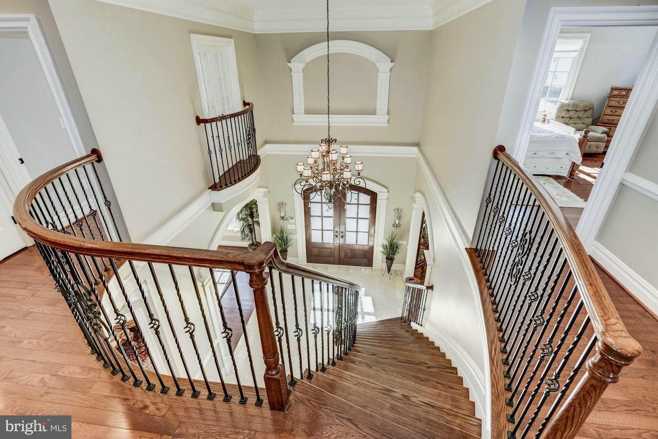 Curved staircase with wooden steps and iron railings, leading to double doors, under a chandelier in a two-story foyer.