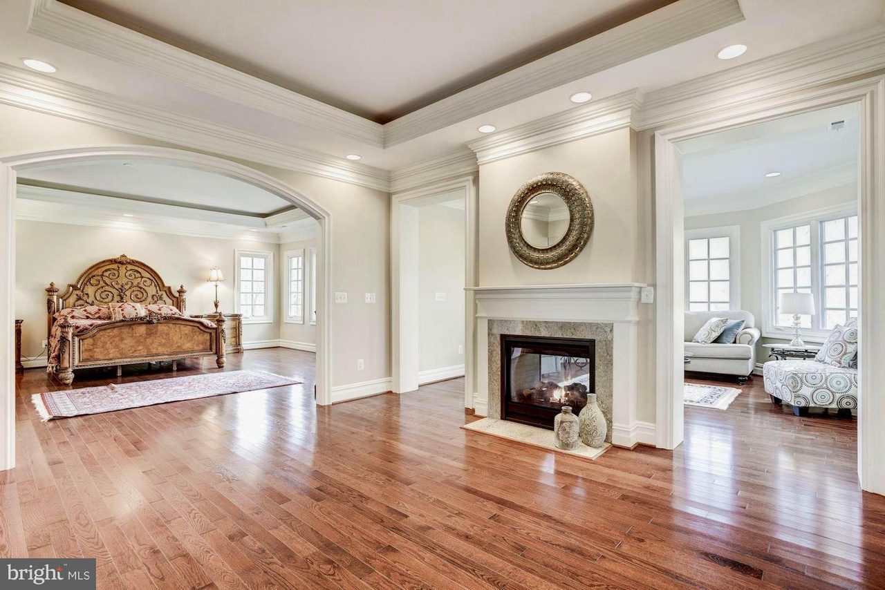 Spacious interior with hardwood floors, a fireplace, an arched opening to a bedroom with a bed, and a sitting area with couches and large windows.