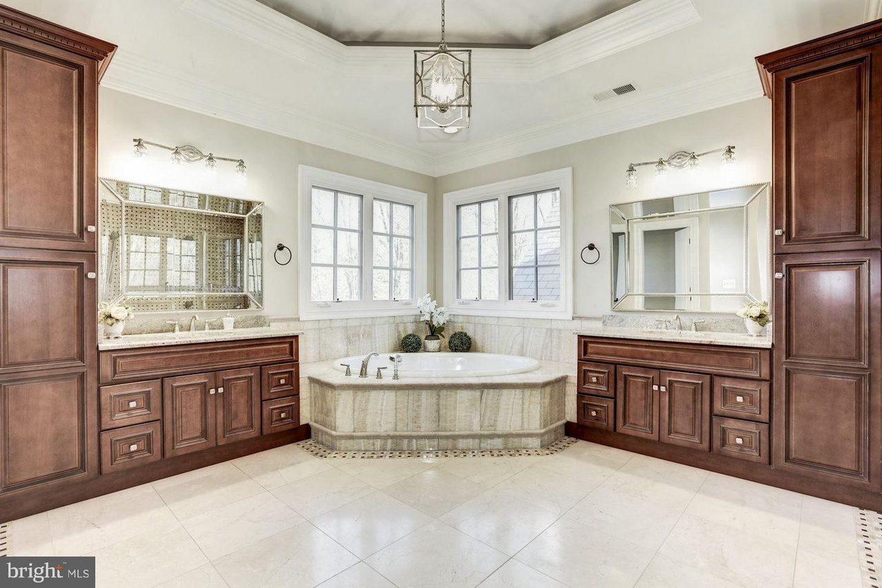 Luxury bathroom with a central bathtub, two large mirrors above double vanities, dark wood cabinetry, chandelier lighting, and tile flooring.