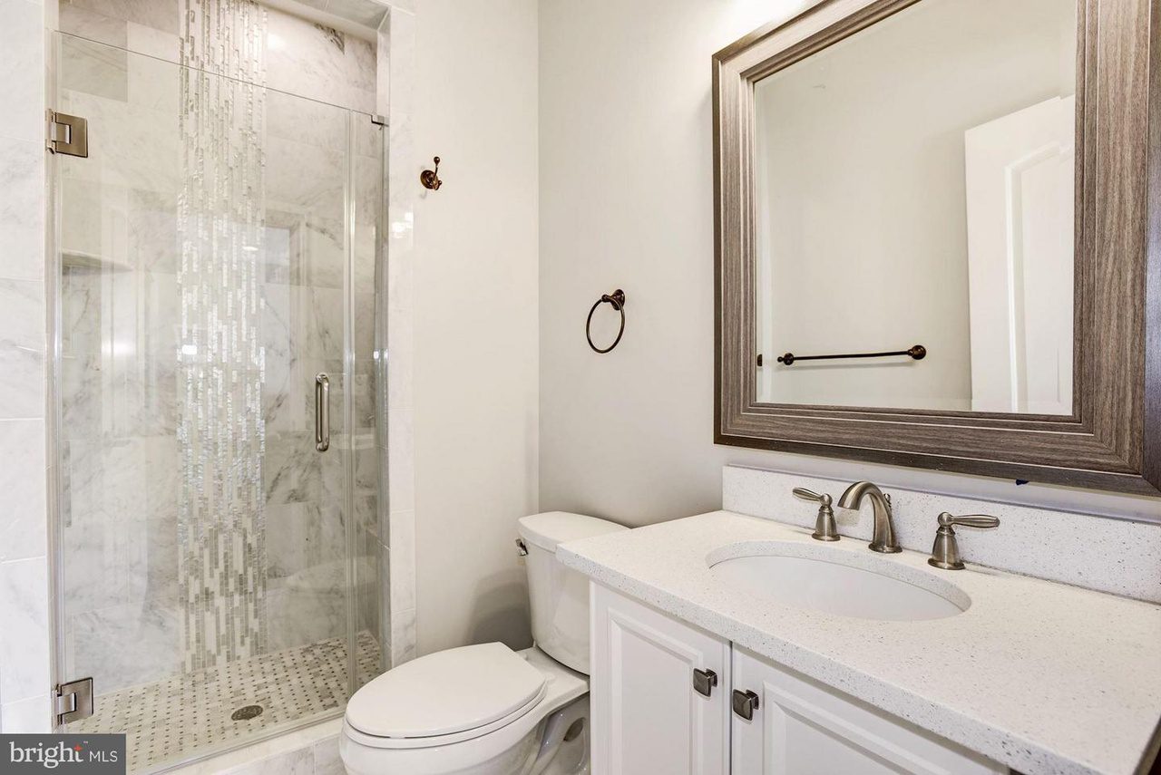 Modern bathroom with a glass-enclosed shower, white countertop sink, toilet, and large rectangular mirror in a wood frame.