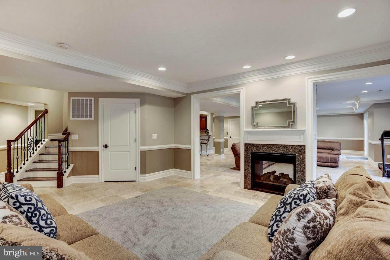 Spacious basement with beige walls, recessed lighting, a fireplace, sectional sofas, and visible stairway. Multiple doorways lead to other rooms.