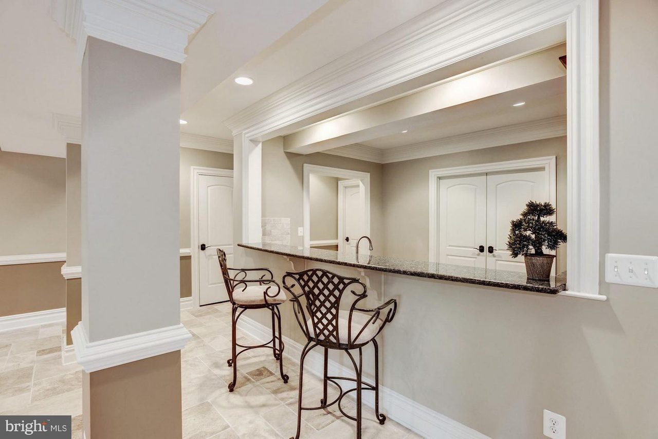 Home interior with a granite countertop bar and two metal chairs, recessed lighting, and white doors. Cream walls and light tiled floor create a neutral ambiance.
