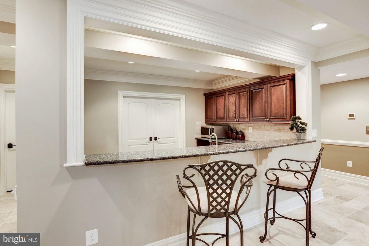 A kitchen bar with two wrought iron chairs, granite countertop, and dark wooden cabinets.