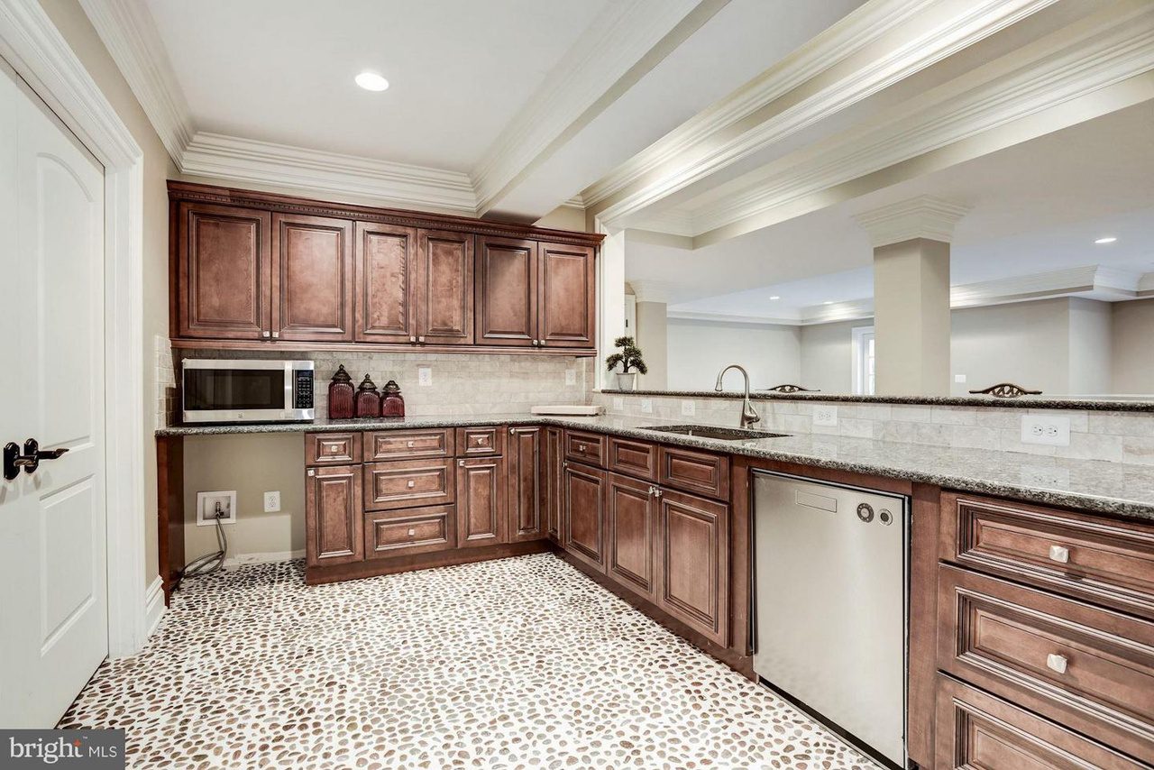 Kitchen with dark wood cabinets, marble countertop, built-in microwave, and patterned flooring. Includes a sink, dishwasher, and decorative vases on the counter against a light wall.