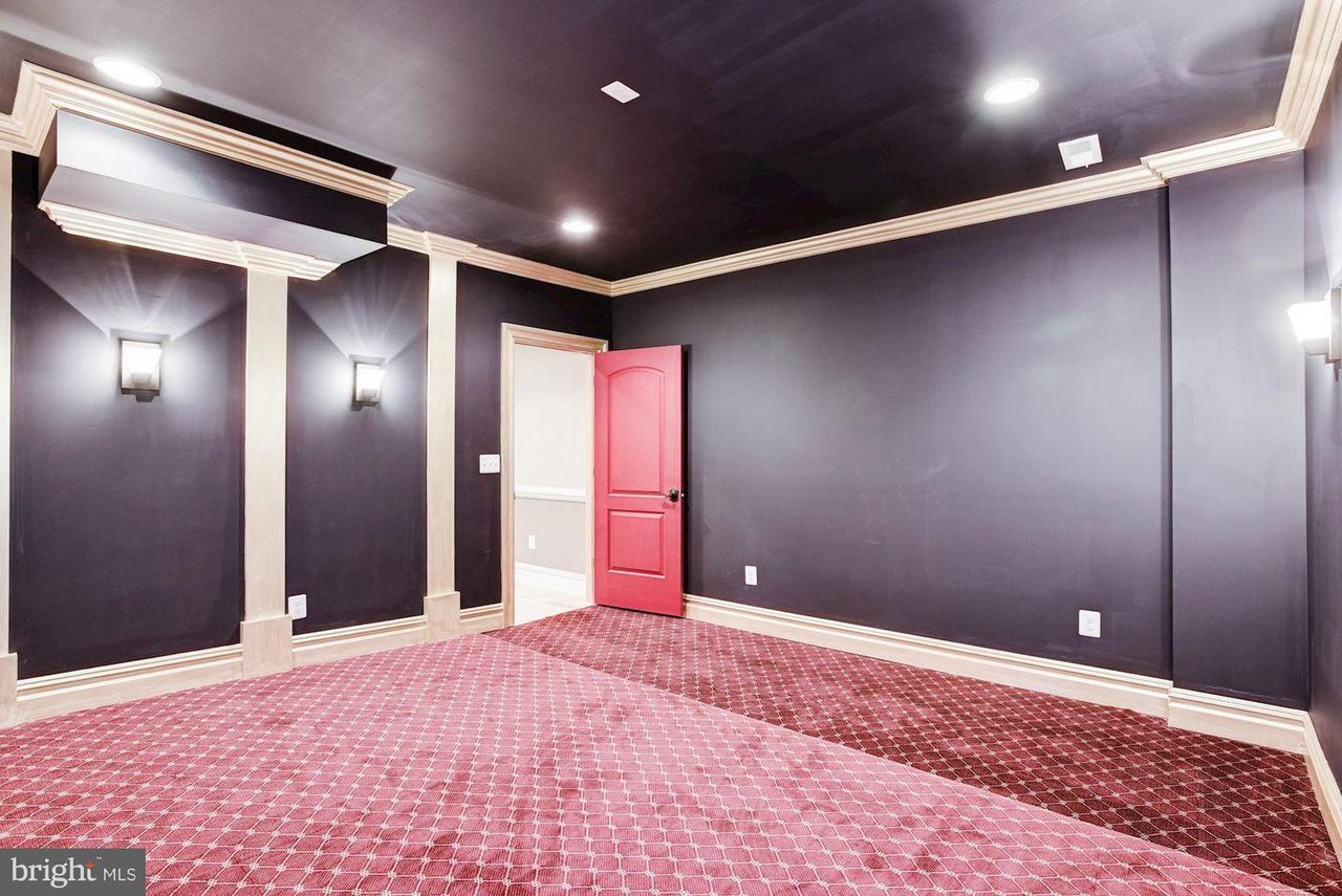 Room with dark walls, beige trim, red patterned carpet, and a red door. Two wall sconces provide lighting.