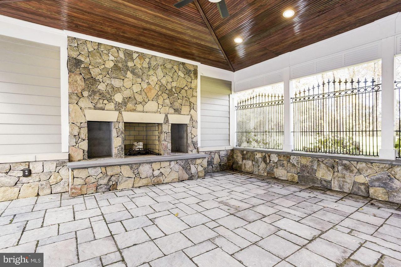 Outdoor patio with a stone fireplace, tiled floor, wood-paneled ceiling, and iron railing.