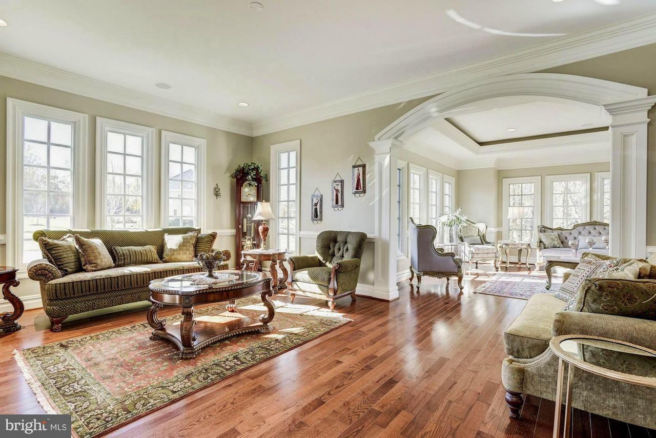 Spacious, sunlit living room with hardwood floors, traditional furniture, arched entryway, and large windows.